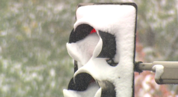 A traffic light covered in snow during a snowfall, with the red light visible through the snow.