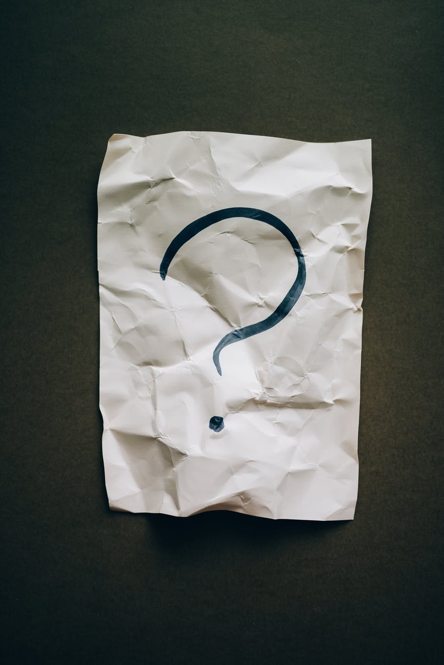 A crumpled piece of white paper with a large, dark question mark drawn in the center, set against a dark background.