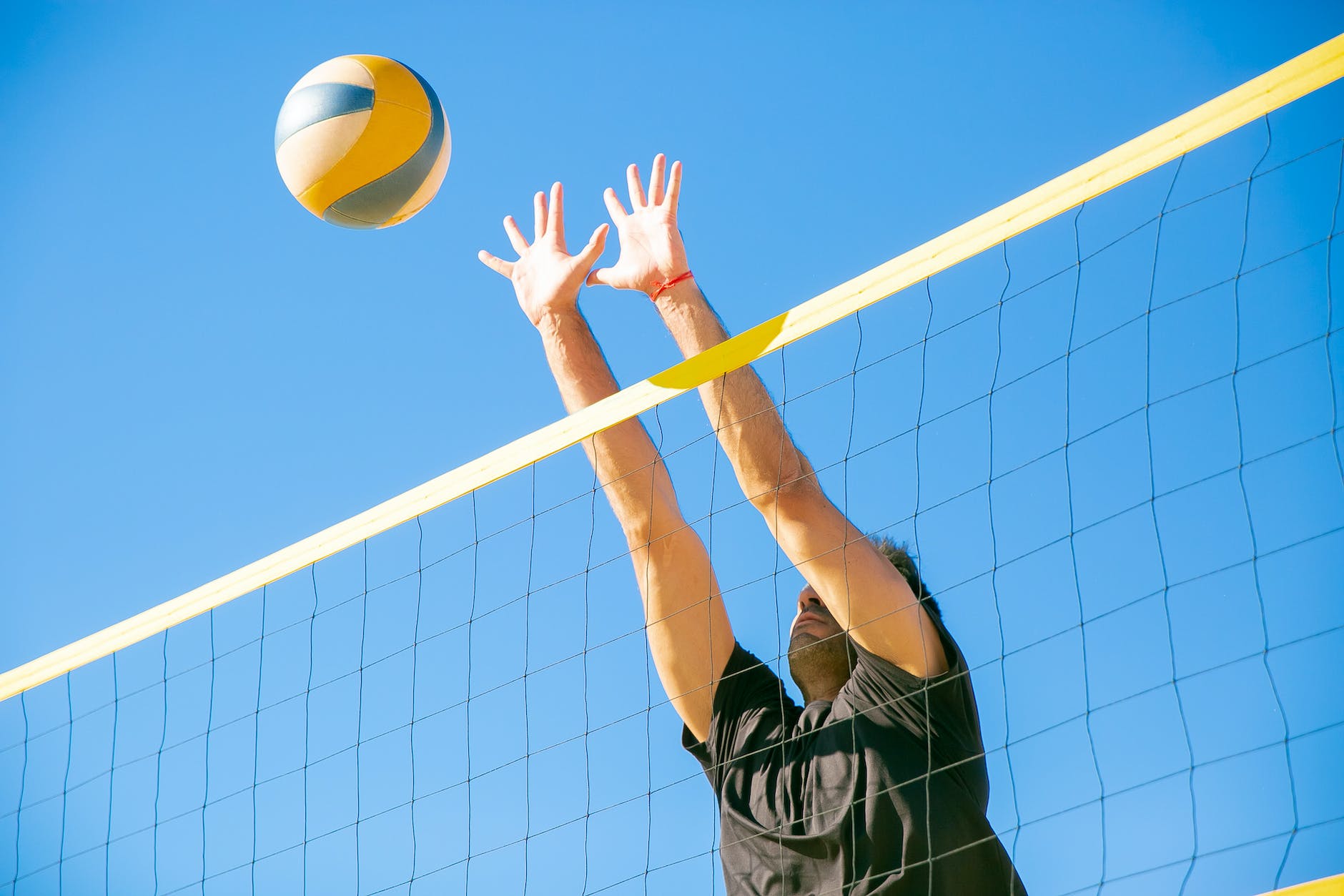 A person jumping to hit a volleyball over a net with a clear blue sky in the background.